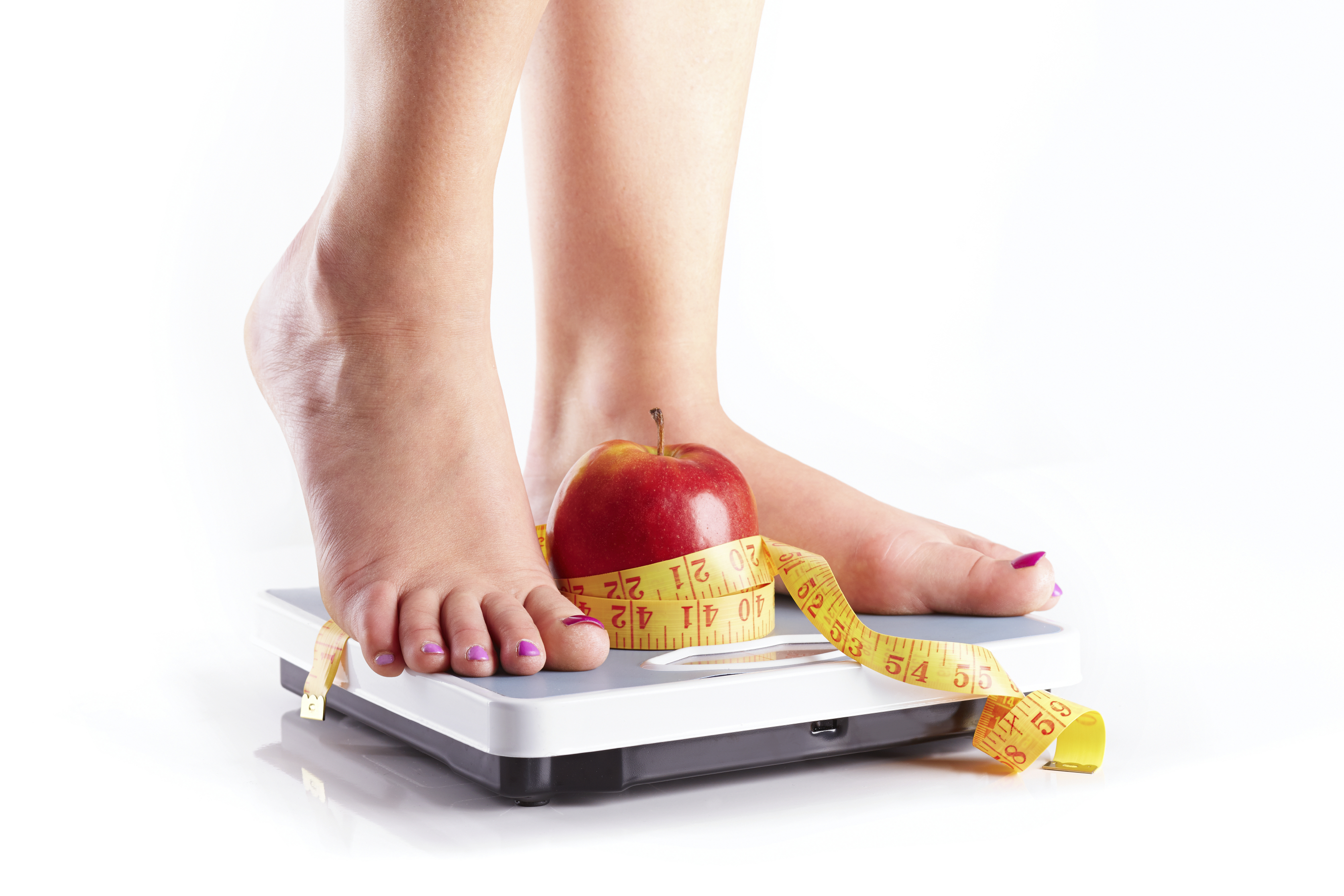 A pair of female feet standing on a bathroom scale with red appl